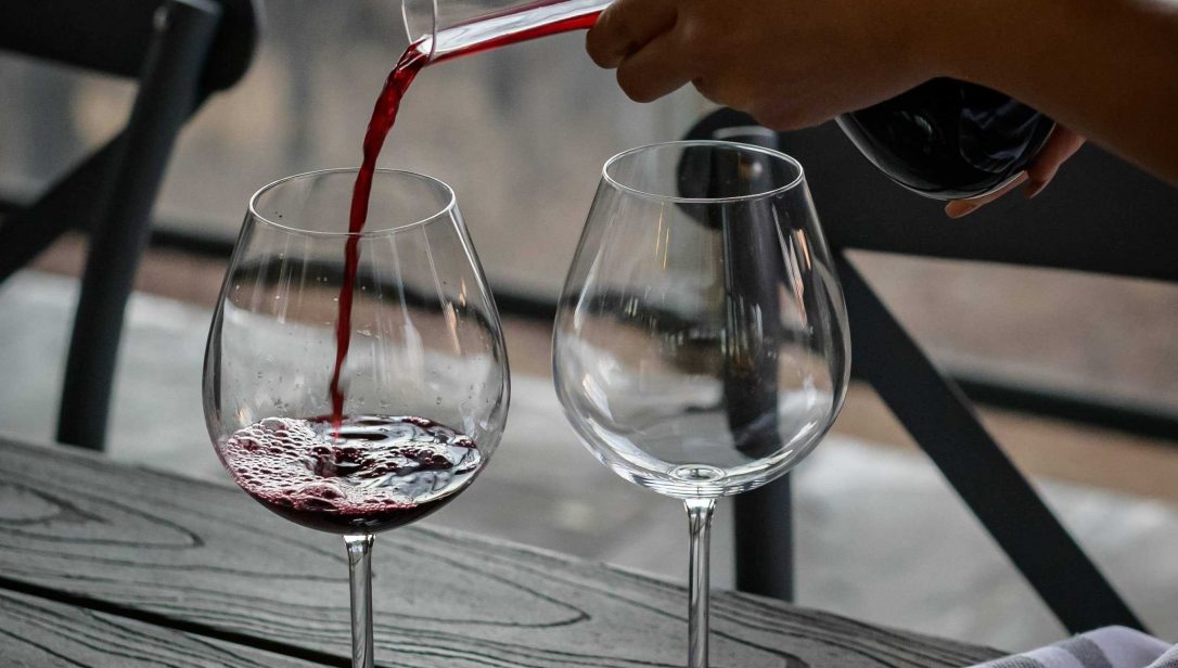 Person pouring red wine into wine class from decanter